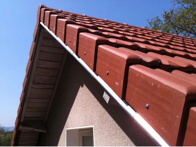 ue en contre-plongée d'un pignon de maison avec tuiles de rive mécaniques et profilé de finition en zinc brillant. Travail de zinguerie soigné sous un ciel bleu