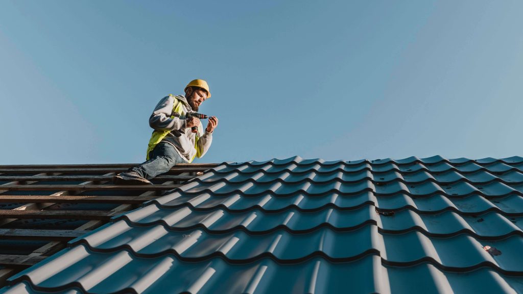 Avis Couvreur professionnel installant des tuiles sur une toiture inclinée avec perceuse, travaux de rénovation de toiture
